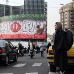 Žena čeka prijelaz ulice pokraj irske zastave i natpisa Zemlja nade u Teheranu, veljača 2025.