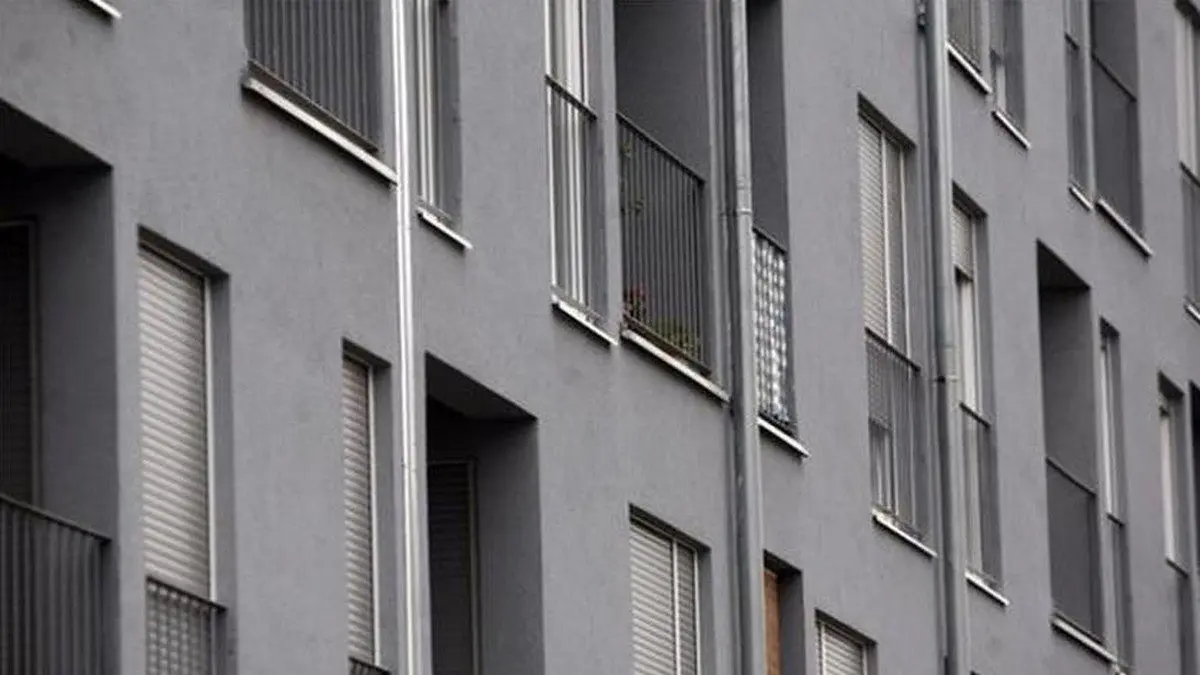 Siva stambena zgrada s balkonima i zatvorenim roletama, simbolizira urbani najam stanova
