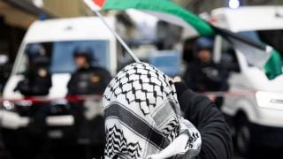 Prosvjednik s kefijom i palestinskom zastavom suočava se s policijom tijekom nedozvoljenog pro-palestinskog skupa u Bernu, 11. listopada 2025.