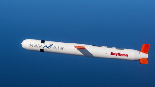 Projektil Tomahawk u letu iznad mora, u visokoj rezoluciji, s jasno vidljivim oznakama „NAV AIR“ i „Raytheon“ na trupu.