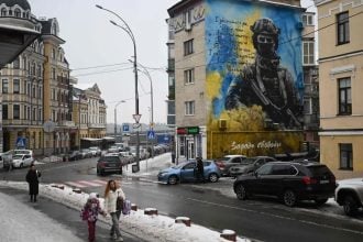 Pješaci prolaze pokraj stambene zgrade s domoljubnim muralom ukrajinskog vojnika u Kijevu tijekom ruske invazije na Ukrajinu, 28. siječnja 2026.