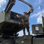 Američki vojnik stoji uz raketni sustav Himars na vojnom vozilu i rukuje lanserom pod vedrim nebom.