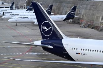 Logo Lufthanse na repovima zrakoplova u zračnoj luci Frankfurt, dok u pozadini leti avion